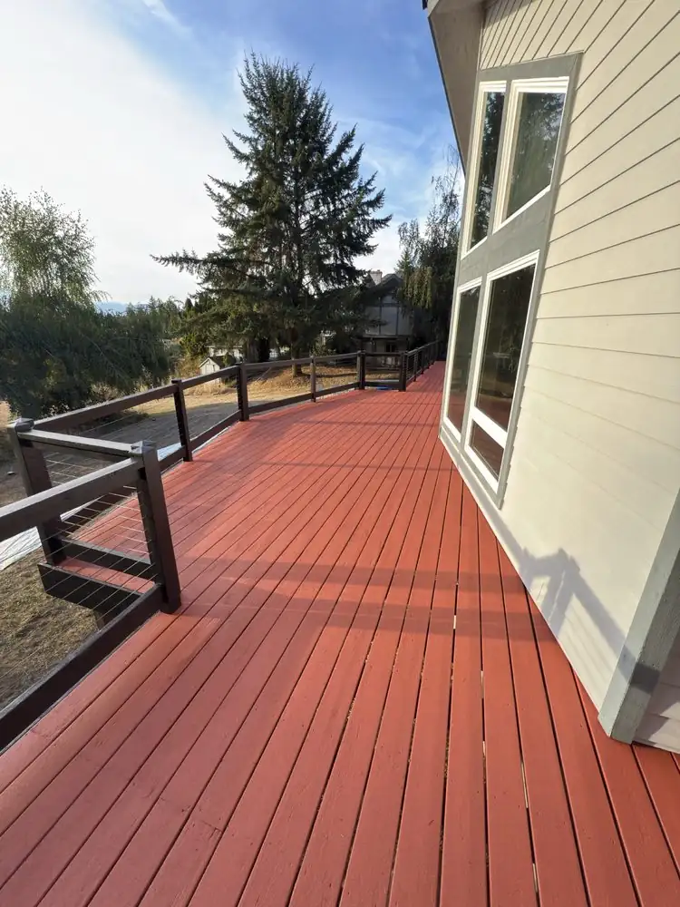 Red-finished deck boards beside a house with cable railing